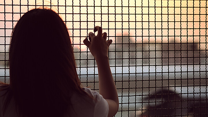 Young girl peers out toward freedom from behind a caged fence