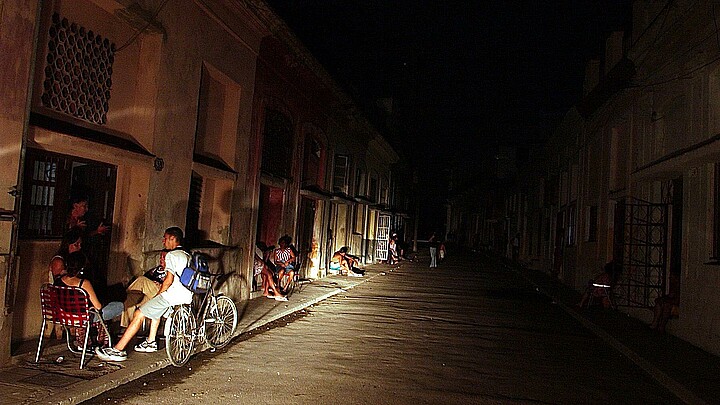 Varias personas conversan iluminadas por la luz de un automóvil en una calle del barrio El Cerro (La Habana) durante un apagón 