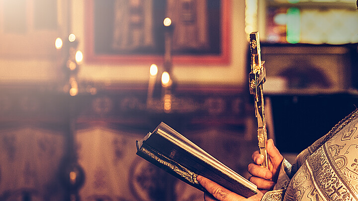 Priest praying in the church holding holly bible and cross