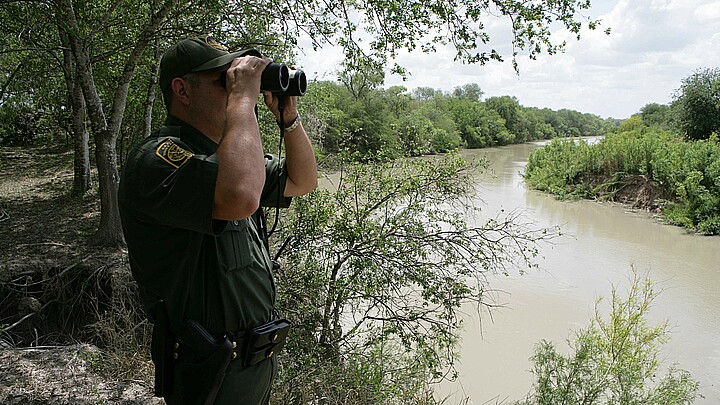 A U.S. Customs Border Patrol agent scans an area into Mexico while searching for potential border crossers