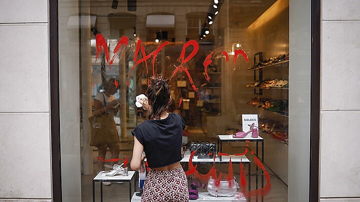 A storekeeper cleans a Macron graffiti written on the storefront in Paris, France, 30 June 2023