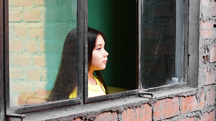 Stock photo of young girl peering out window in Latin America