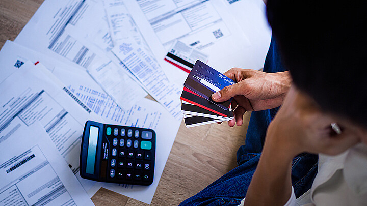 Una calculador sobre hojas regadas en mesa y en la mano cuatro tarjetas de crédito