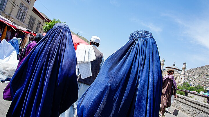 Two women in blue burqas walk on a street in Kabul, Afghanistan