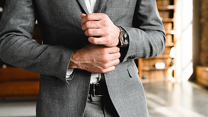 Foto recortada del próspero hombre de negocios tocando sus mangas de esmoquin en la oficina. Gerente jefe millonario arreglando traje formal en el lugar de trabajo. Reloj de pulsera caro