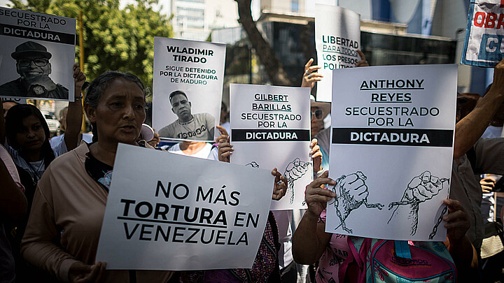 Fotografía de archivo de personas con carteles que muestran imágenes de detenidos durante una manifestación frente a la sede del Ministerio de Servicio Penitenciario, en Caracas. 