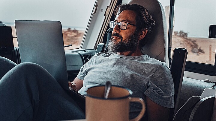 Nómada digital nuevo estilo de vida moderno de trabajo con un hombre adulto atractivo trabajando y relajándose dentro de una camioneta de camper con playa y naturaleza afuera