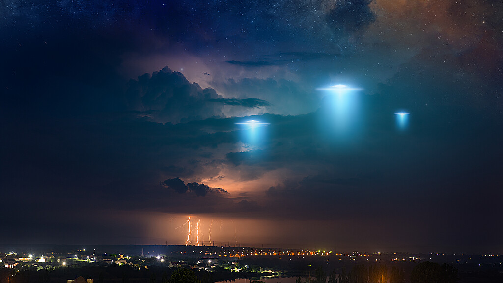 Amazing fantastic background - extraterrestrial aliens spaceship fly above small town, ufo with blue spotlights in dark stormy sky. Elements of this image furnished by NASA.