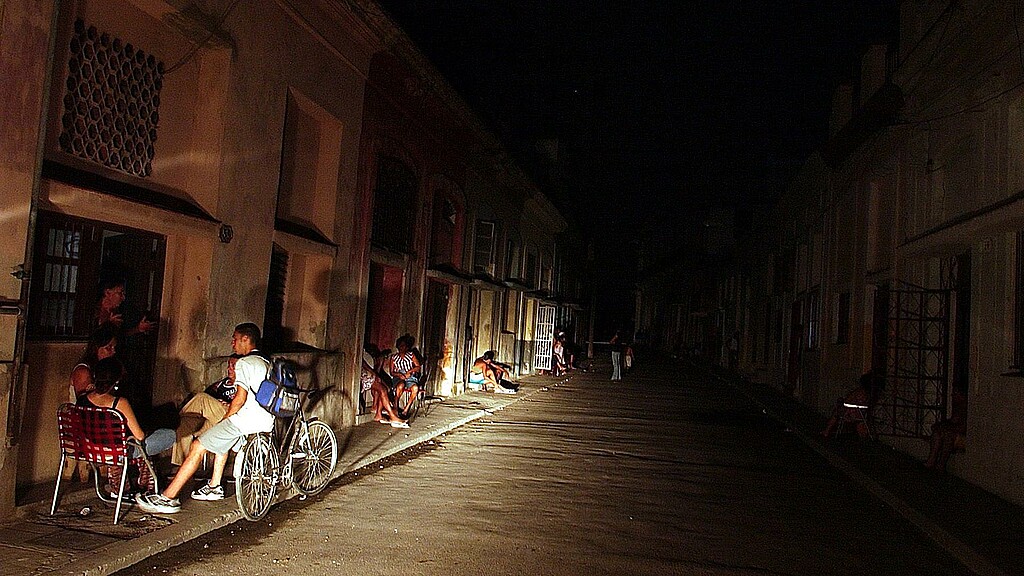Varias personas conversan iluminadas por la luz de un automóvil en una calle del barrio El Cerro (La Habana) durante un apagón 