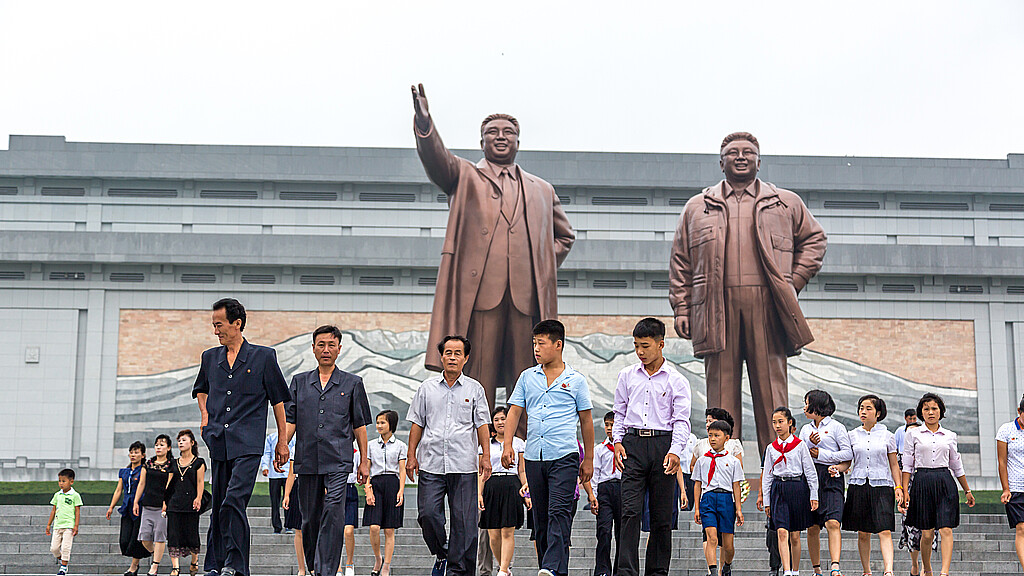 Ciudadanos paseando frente a una gran estatua en Pyongyang, capital de Corea del Norte