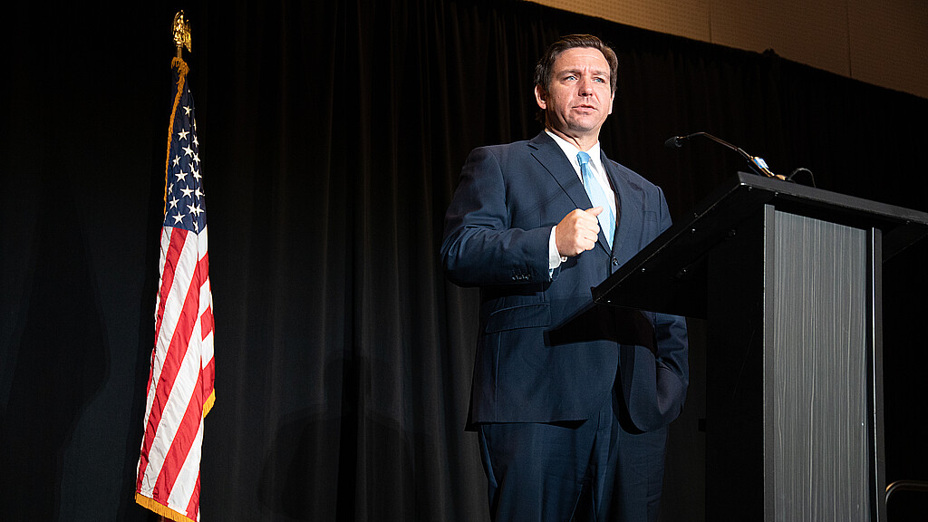 Florida Gov. Ron DeSantis stands firmly by an American flag while speaking