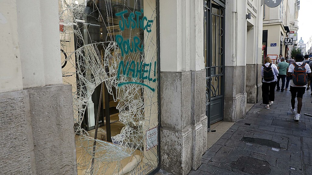 Varias personas pasan por delante de una tienda dañada tras una noche de saqueos y disturbios en Marsella