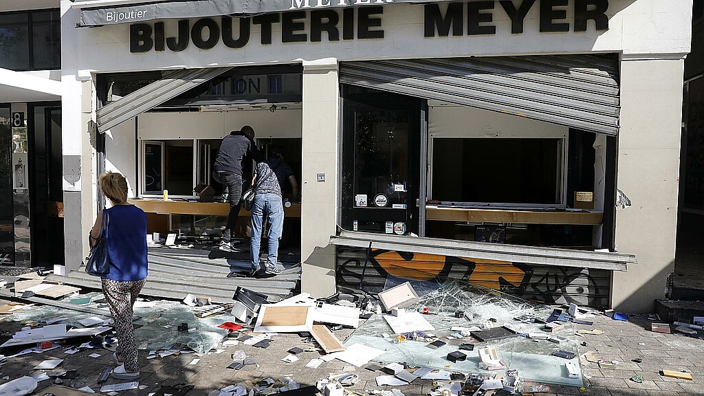 Varias personas pasan por delante de una tienda dañada tras una noche de saqueos y disturbios en Marsella.