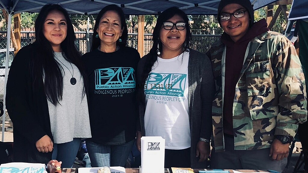 From left to right: Julia Bernal, CEO of Pueblo Action Alliance (PAA), Secretary of the Interior Deb Haaland donning a PAA T-shirt, unidentified woman, Sheldon Tenorio from PAA and the NW Venceremos Brigade