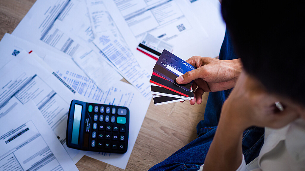 Una calculador sobre hojas regadas en mesa y en la mano cuatro tarjetas de crédito
