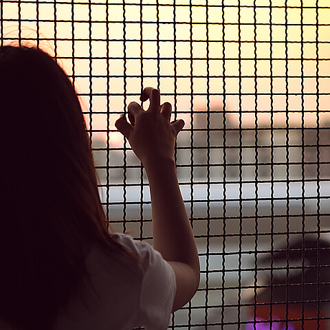 Young girl peers out toward freedom from behind a caged fence