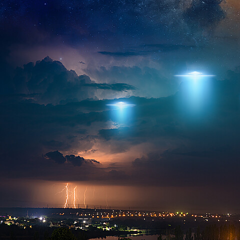 Amazing fantastic background - extraterrestrial aliens spaceship fly above small town, ufo with blue spotlights in dark stormy sky. Elements of this image furnished by NASA.