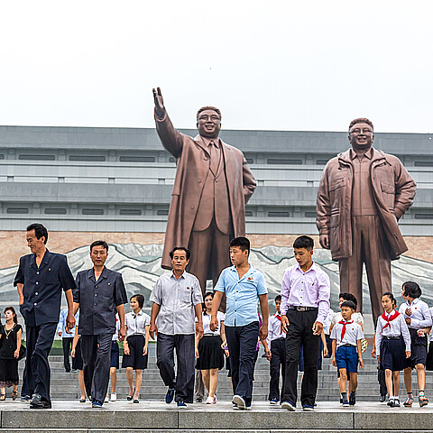 Ciudadanos paseando frente a una gran estatua en Pyongyang, capital de Corea del Norte