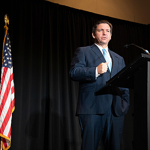 Florida Gov. Ron DeSantis stands firmly by an American flag while speaking