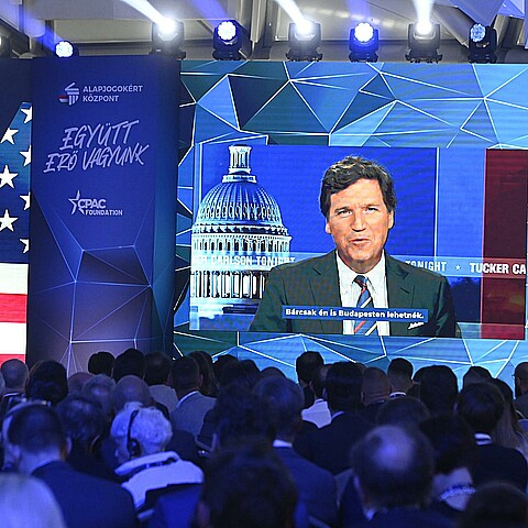 American media personality Tucker Carlson appears on the screen as he delivers his video message on the first day session of the Conservative Political Action Conference (CPAC) Hungary