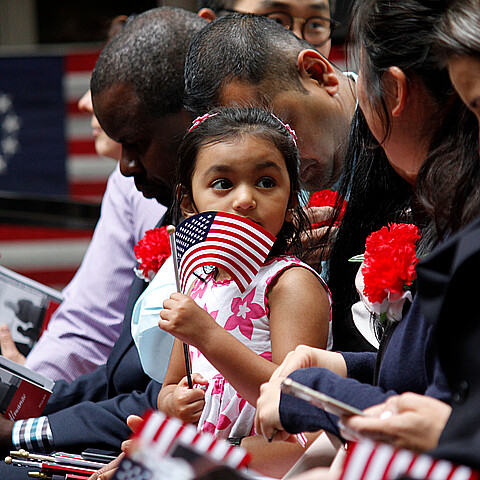 The daughter of an immigrant holds an American flag while she joins her mother's naturalization ceremony on Flag Day at the historic Betsy Ross House in Philadelphia