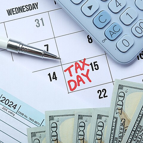 Calendario con dia de impuestos, una calculadora y seis billetes de 100 dólares