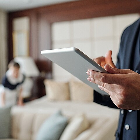 Cierre de un joven gerente de hotel usando tableta digital mientras observa la lista de invitados con camarera en segundo plano