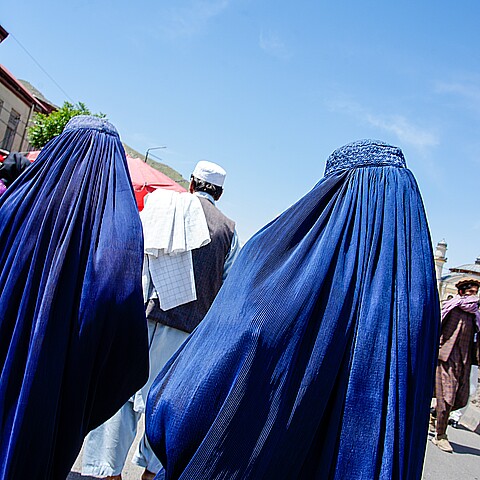 Two women in blue burqas walk on a street in Kabul, Afghanistan