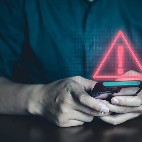 Hombre con un celular en mano y el logo de advertencia