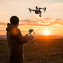 Man operating a drone with remote control. Dark silhouette against colorful sunset.