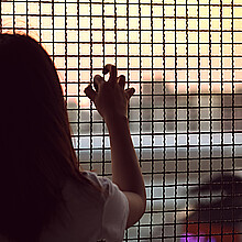Young girl peers out toward freedom from behind a caged fence
