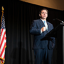 Florida Gov. Ron DeSantis stands firmly by an American flag while speaking