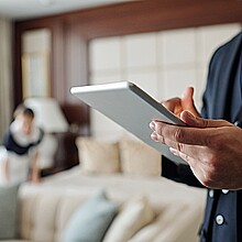Cierre de un joven gerente de hotel usando tableta digital mientras observa la lista de invitados con camarera en segundo plano