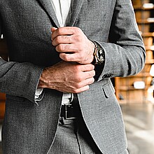 Foto recortada del próspero hombre de negocios tocando sus mangas de esmoquin en la oficina. Gerente jefe millonario arreglando traje formal en el lugar de trabajo. Reloj de pulsera caro