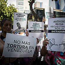 Fotografía de archivo de personas con carteles que muestran imágenes de detenidos durante una manifestación frente a la sede del Ministerio de Servicio Penitenciario, en Caracas. 